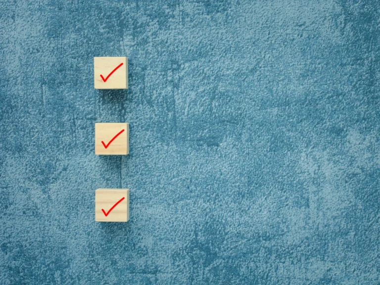 Three wooden blocks with red checkmarks arranged vertically on a textured blue background, representing a completed checklist.