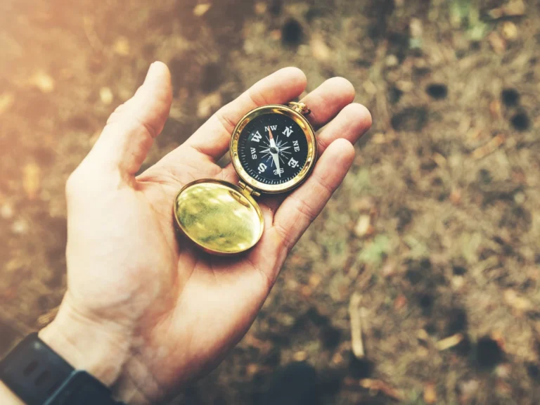An open hand holding a brass compass outdoors, symbolizing guidance and finding direction.