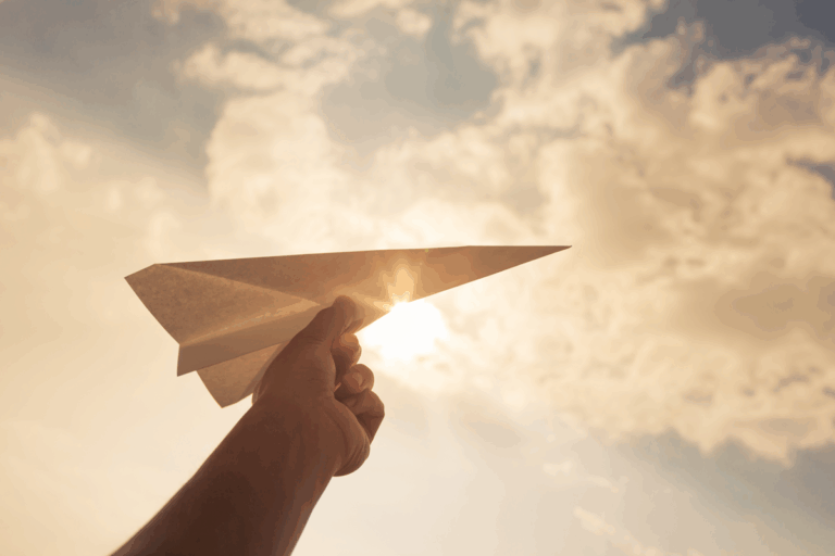 child'shand holding paper plane with sun in the background