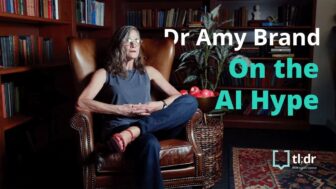 Dr Amy Brand sits in a chair in a library being interviewed