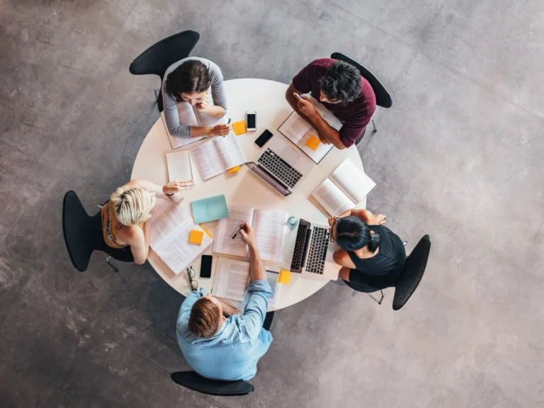 Overhead view of a team collaborating around a table with laptops, documents, and notes, representing partnership-building between industry and research.
