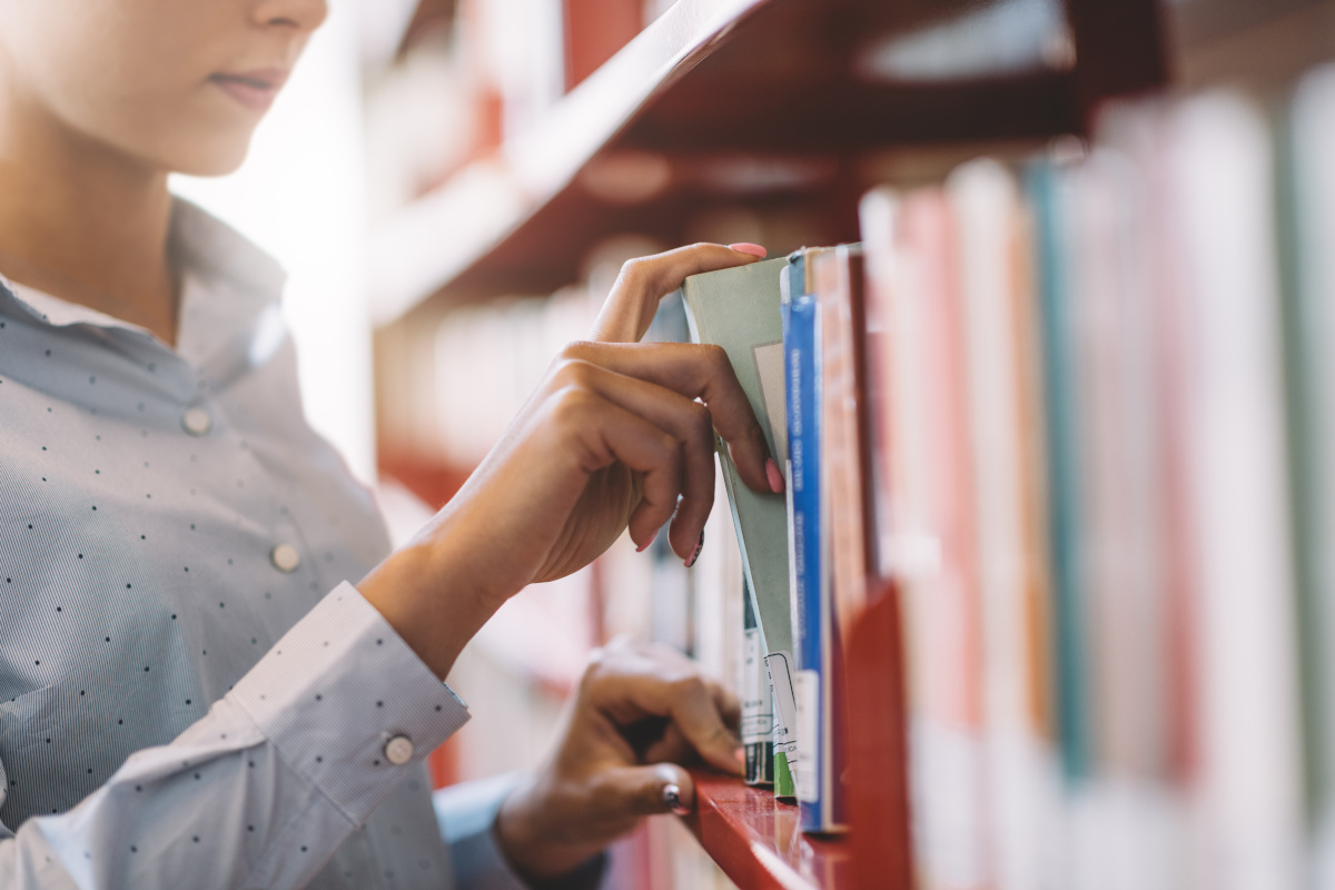 A woman browsing a library bookshelf, pulling a book from the shelf.